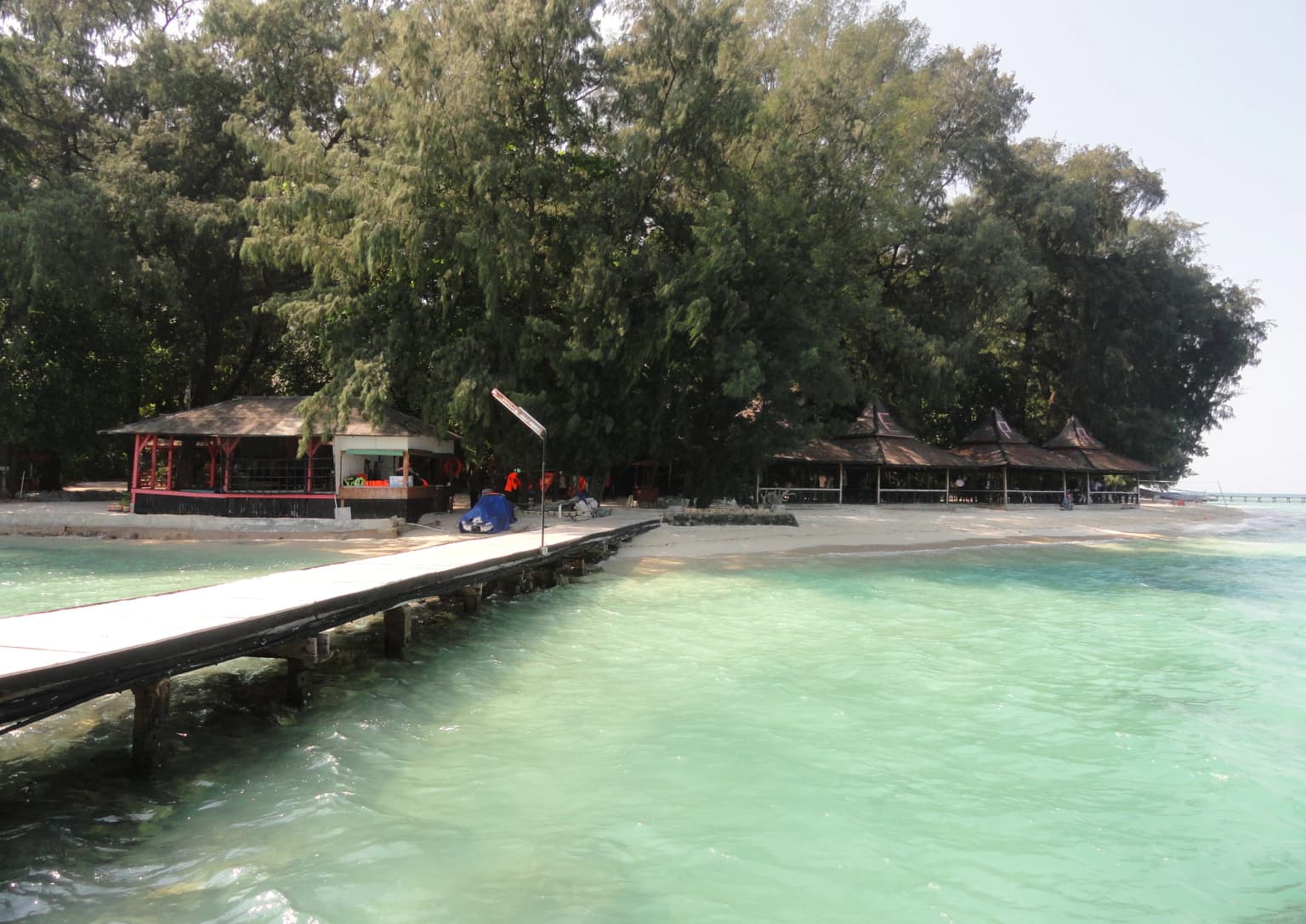 Pier extending into turquoise water with resort buildings and trees on Pulau Sepa, Indonesia