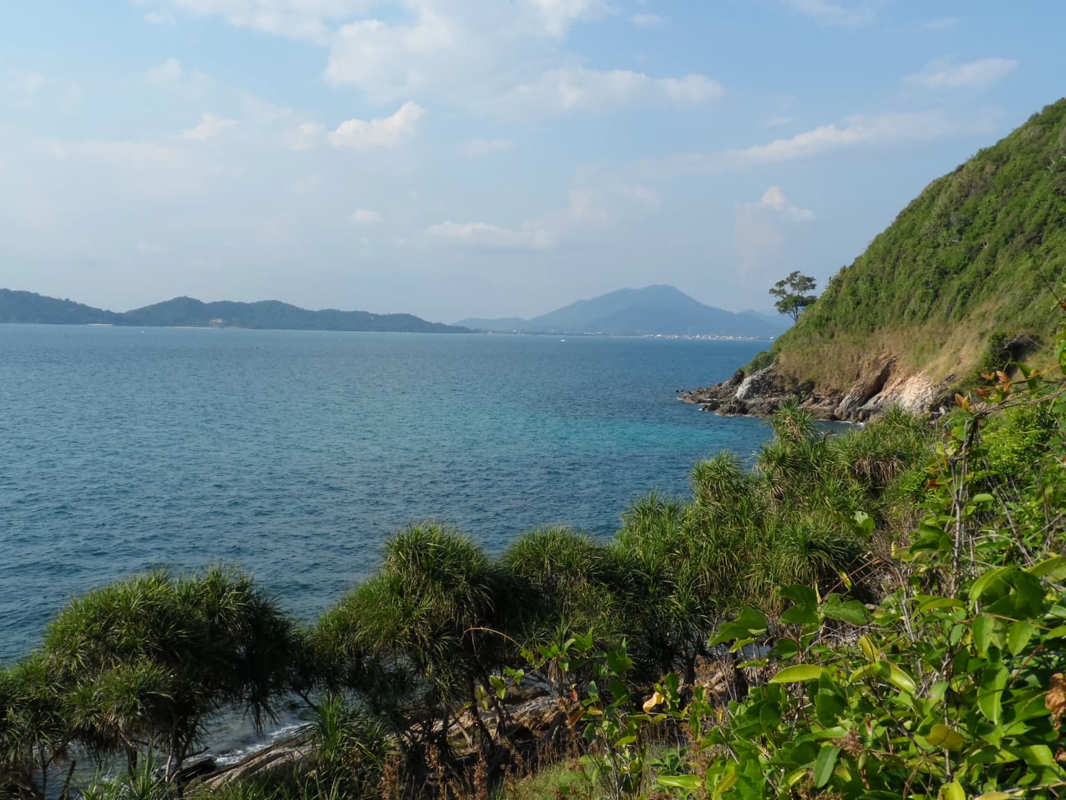 Turquoise ocean waters along the west coast of Ko Samet, with green vegetation and hills in the background