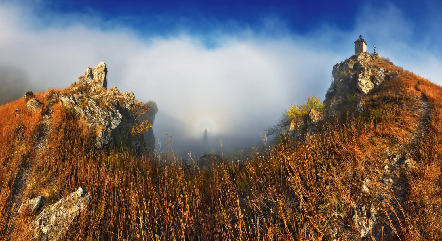 A misty landscape featuring rocky hills, dry grasses, and Khotyn Fortress on a hilltop