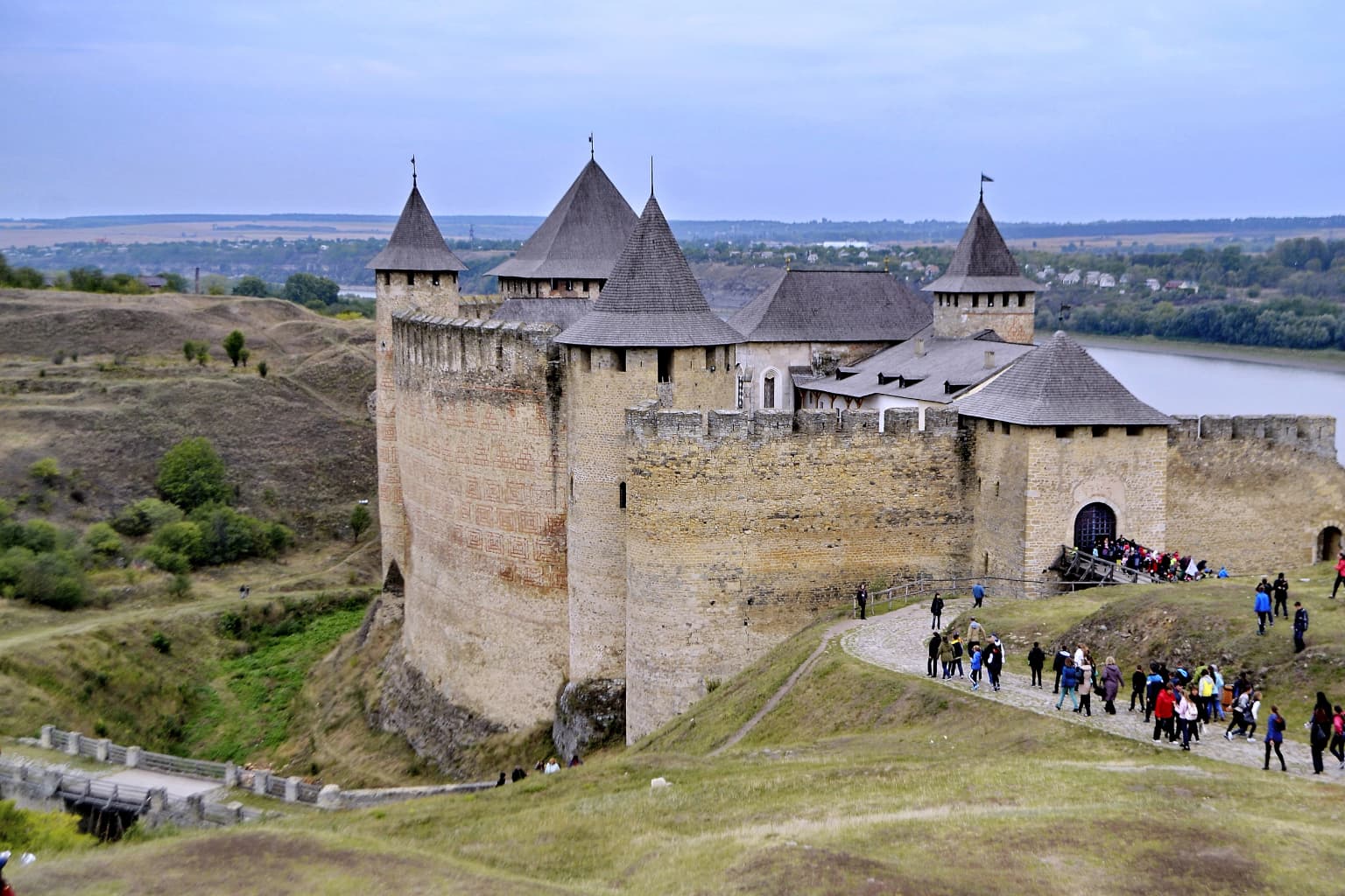Khotyn Fortress on a hillside overlooking the Dniester River with visitors walking along a path