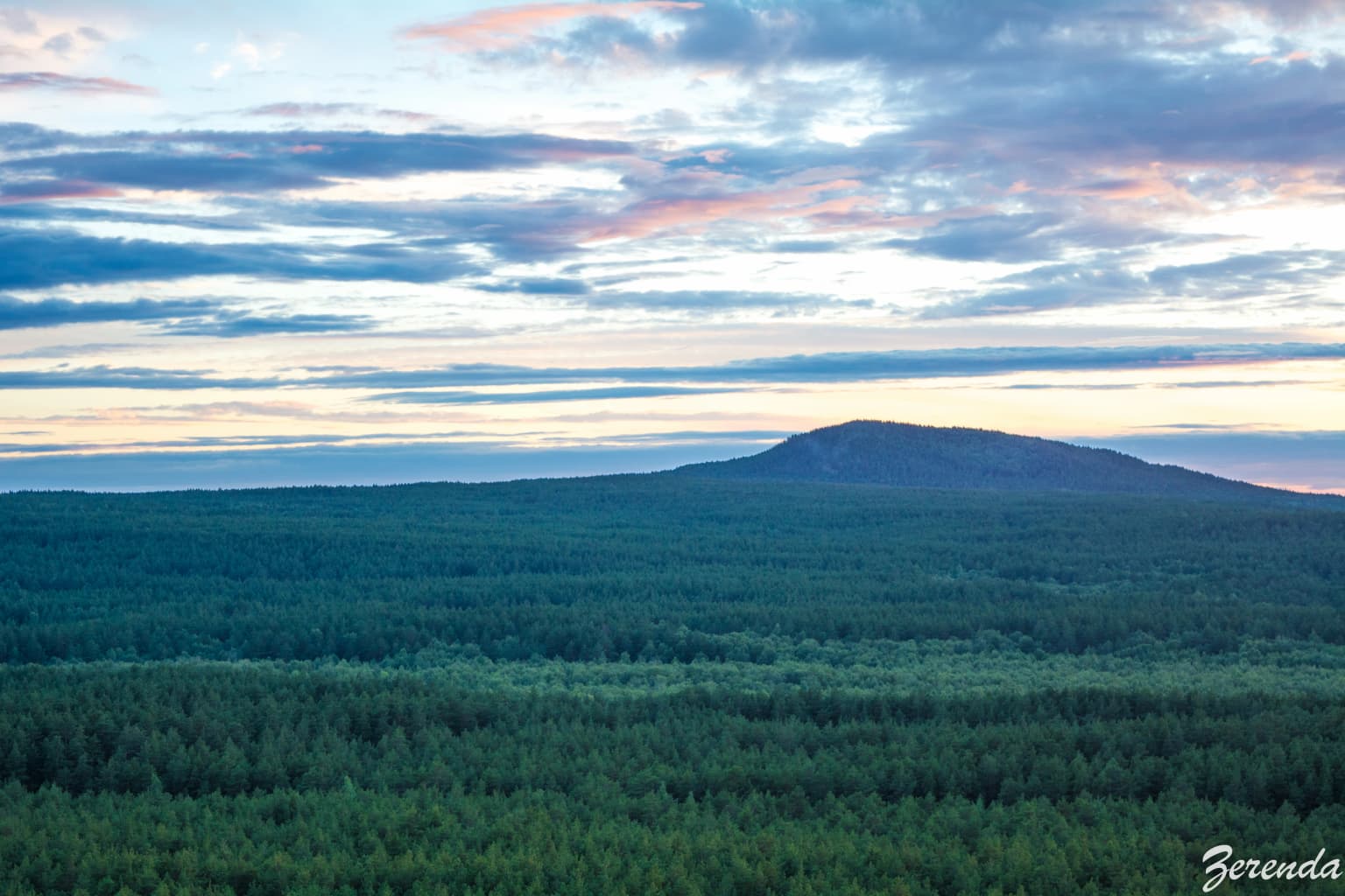 Wide landscape of Bear Hill rising from a dense green forest under a partly cloudy sky with pink and blue hues