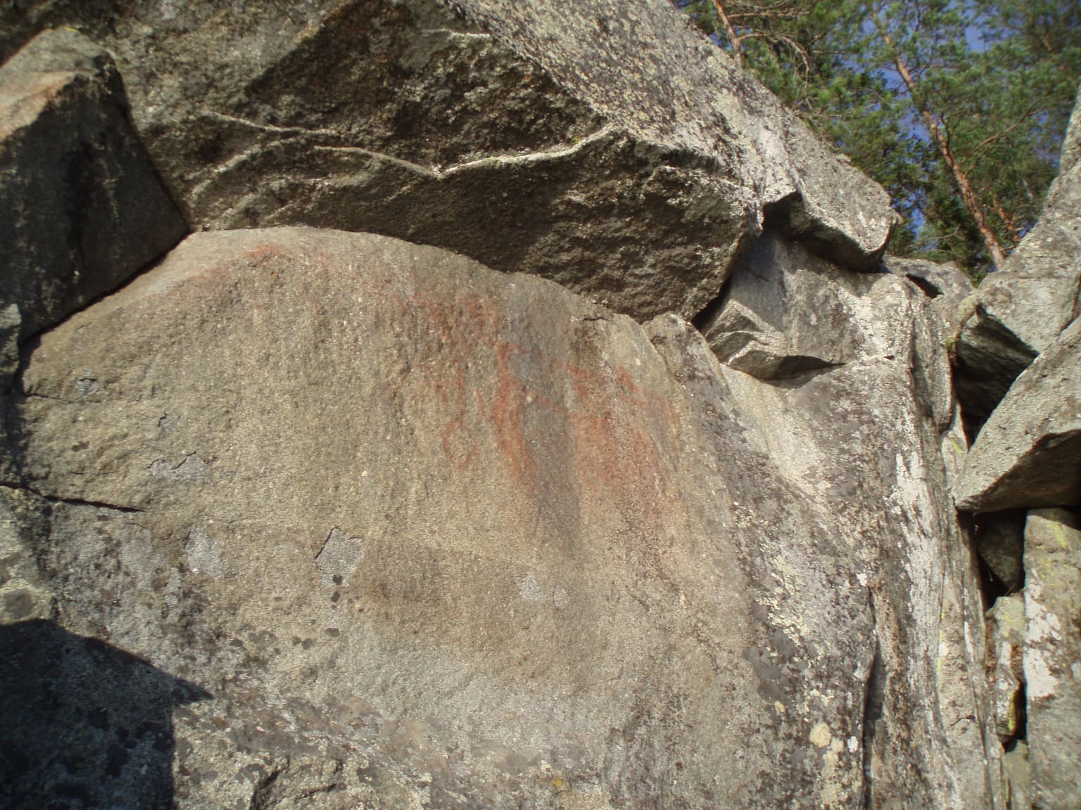 Faint red cave painting on a large gray rock face with surrounding boulders.