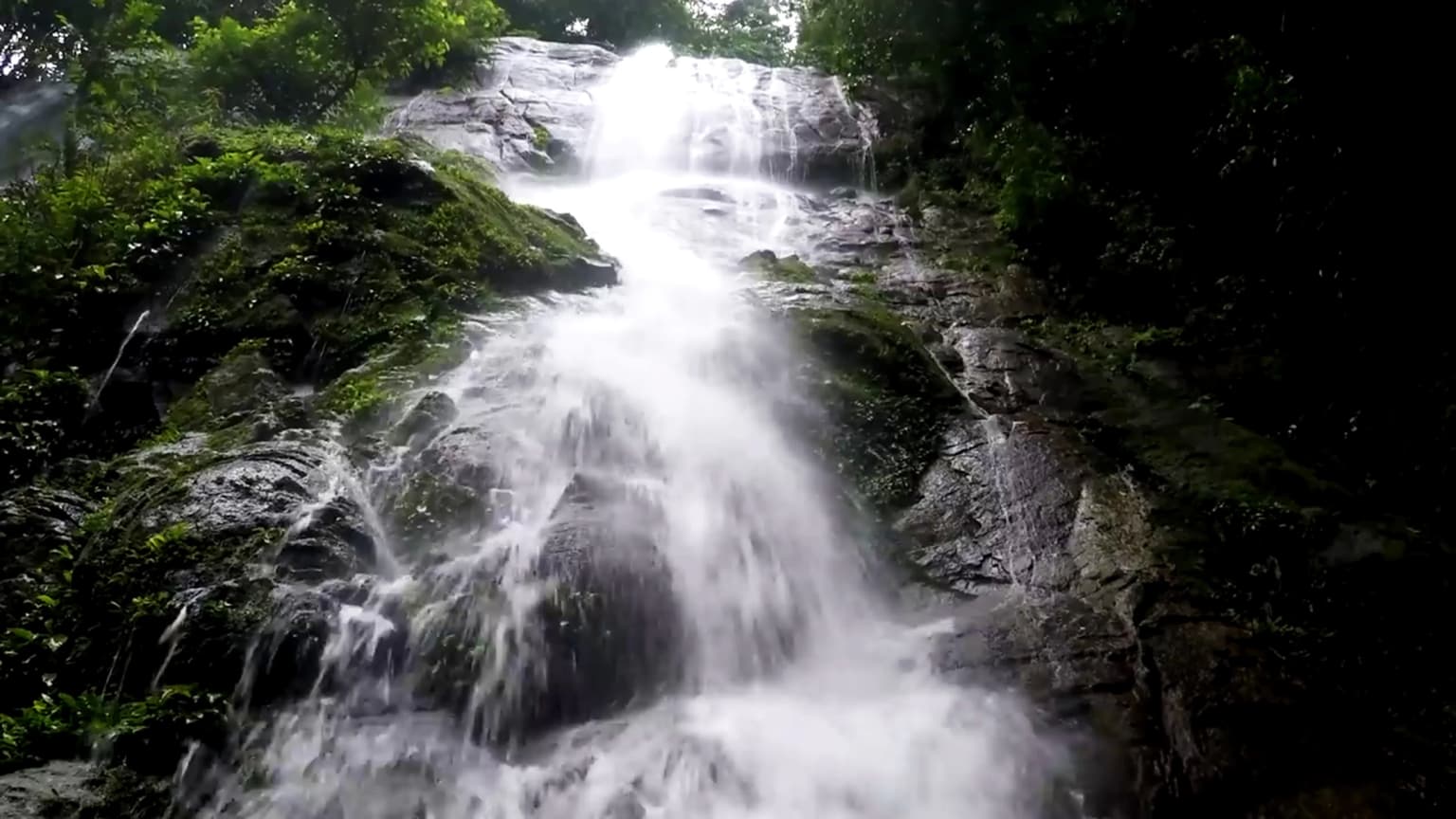Una cascada de varios niveles que fluye sobre rocas oscuras con densa vegetación verde
