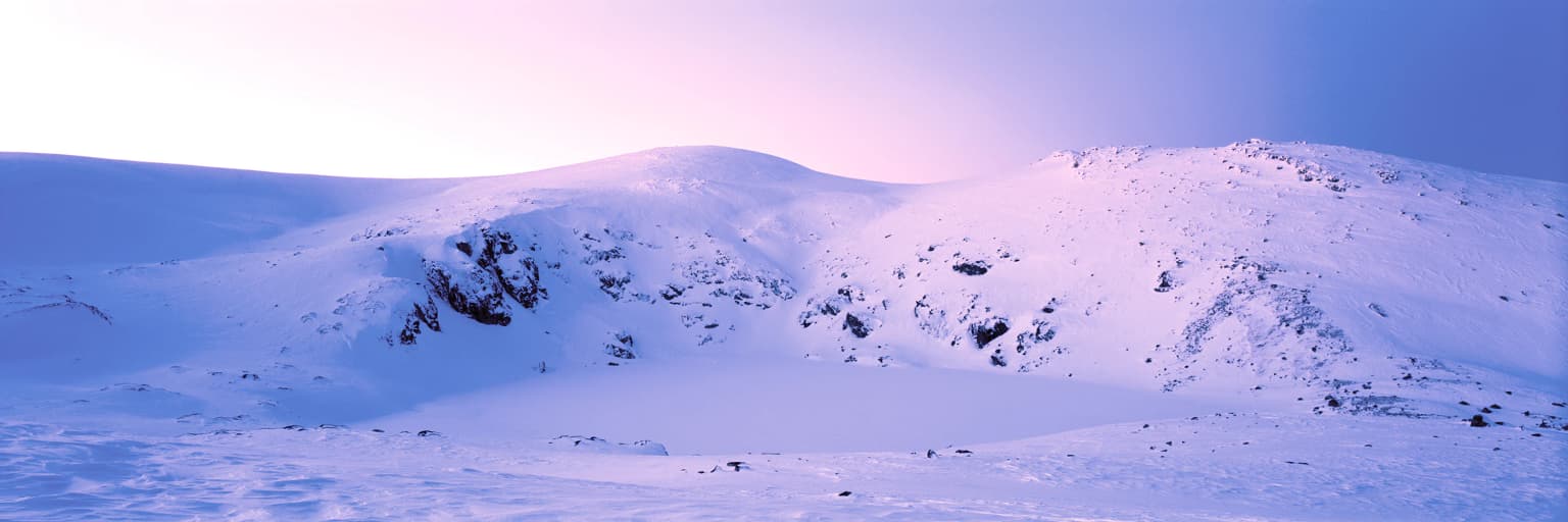 Cordillera montañosa nevada con afloramientos rocosos bajo un cielo rosa pálido