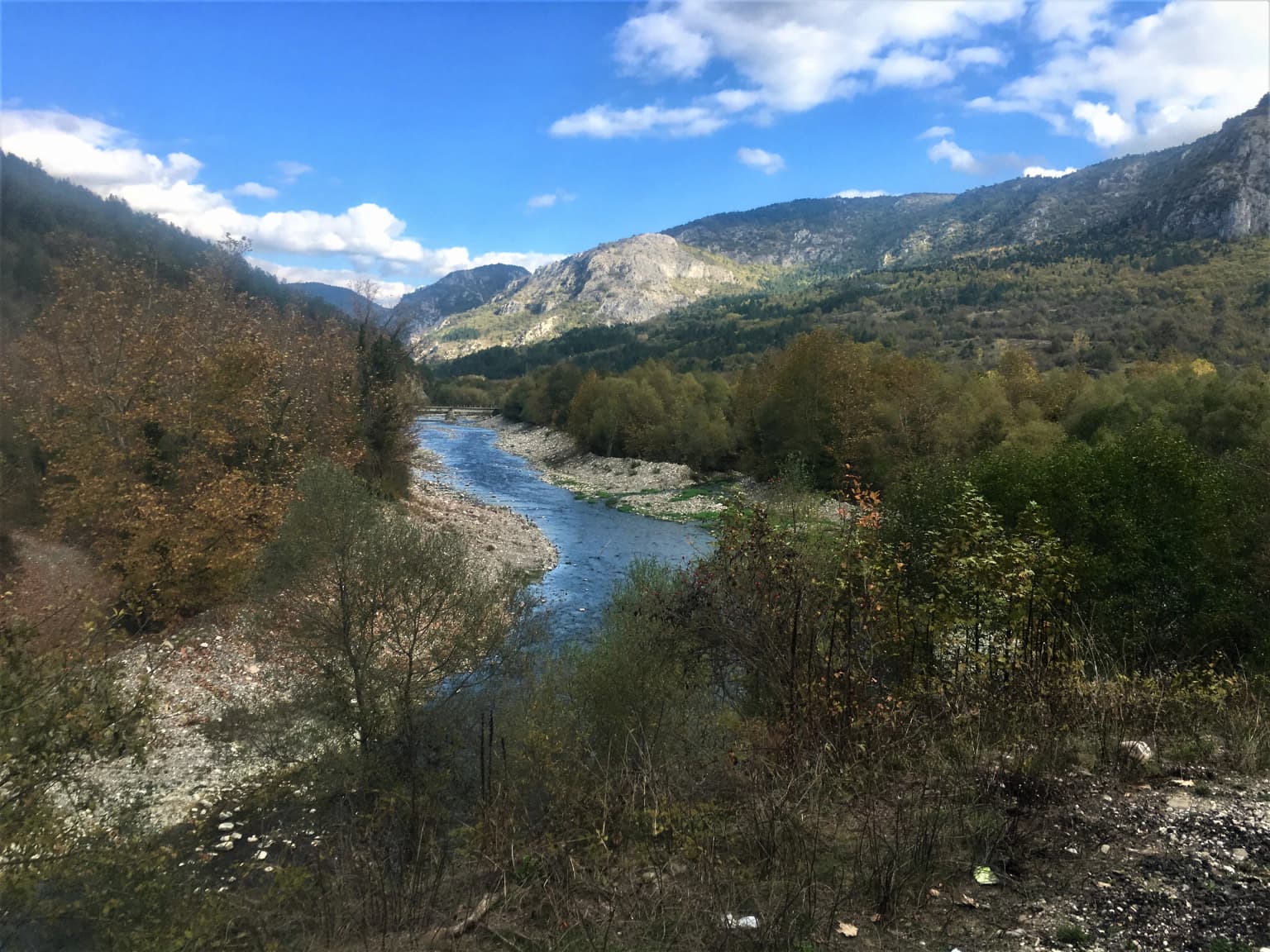 Wide river flowing through valley surrounded by forested mountains under blue sky with scattered clouds