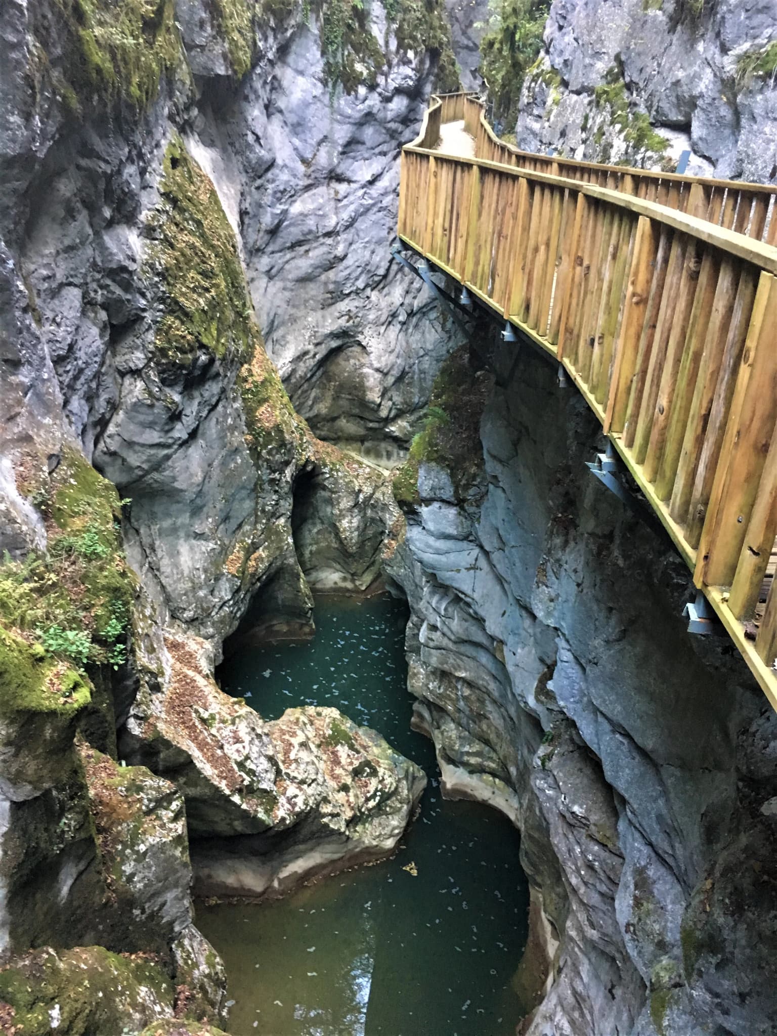 Deep canyon with steep rocky walls, green water at the bottom, and a wooden walkway on the right side