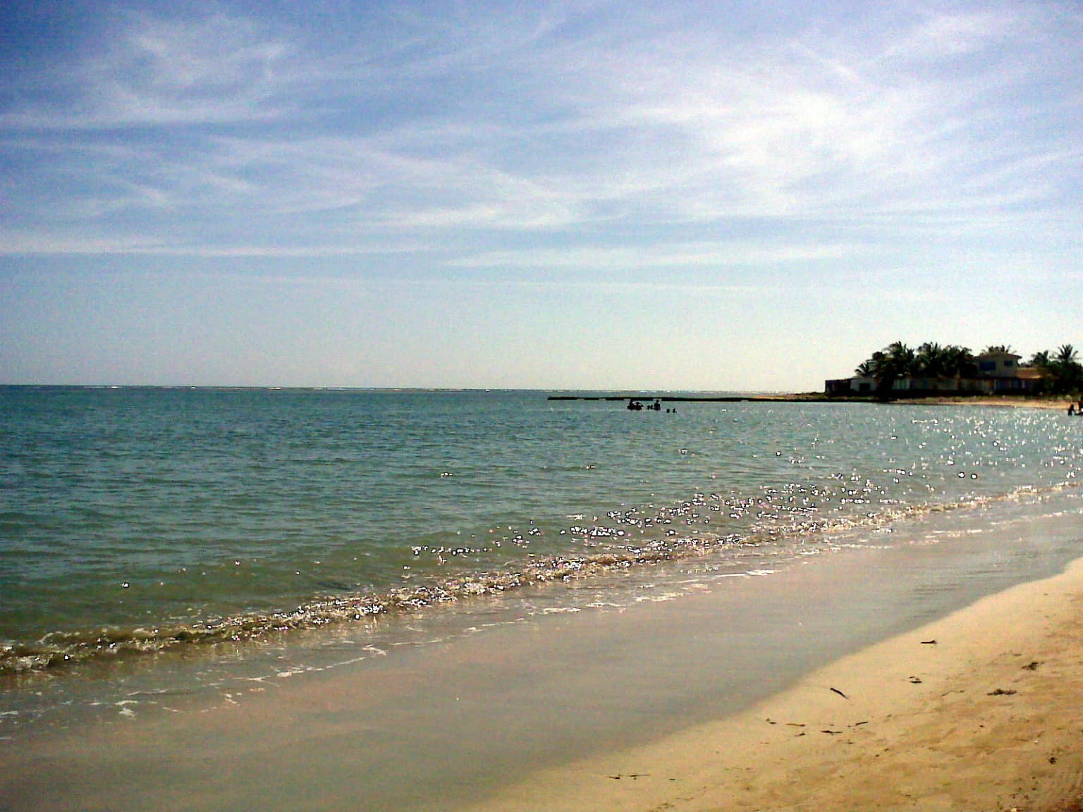 Sandy beach with calm turquoise water extending to the horizon under a partly cloudy sky
