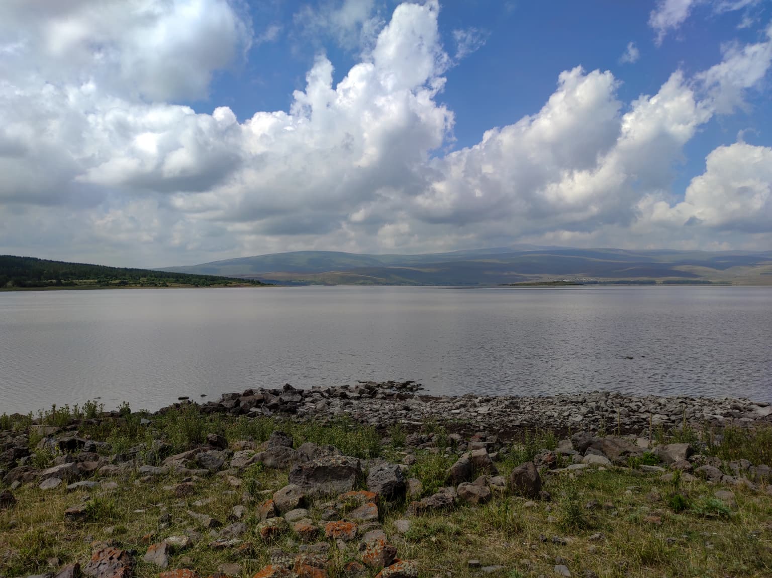 Lake Arpi National Park featuring a large lake with rocky shore, grassy foreground, and mountains in the distance under a partly cloudy sky