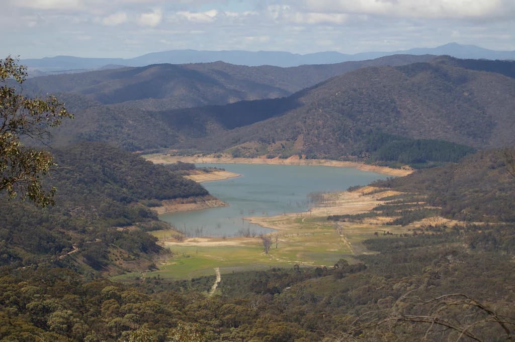 Vista panorámica del lago Eildon con las colinas y montañas circundantes bajo un cielo parcialmente nublado.