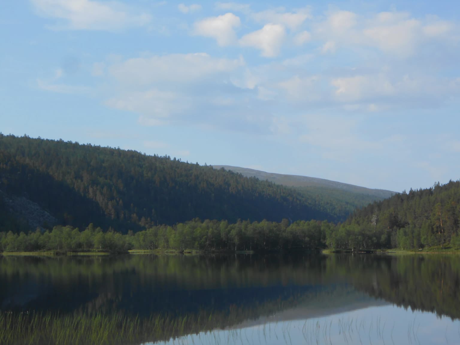 A serene lake reflecting forested mountains under a partly cloudy sky
