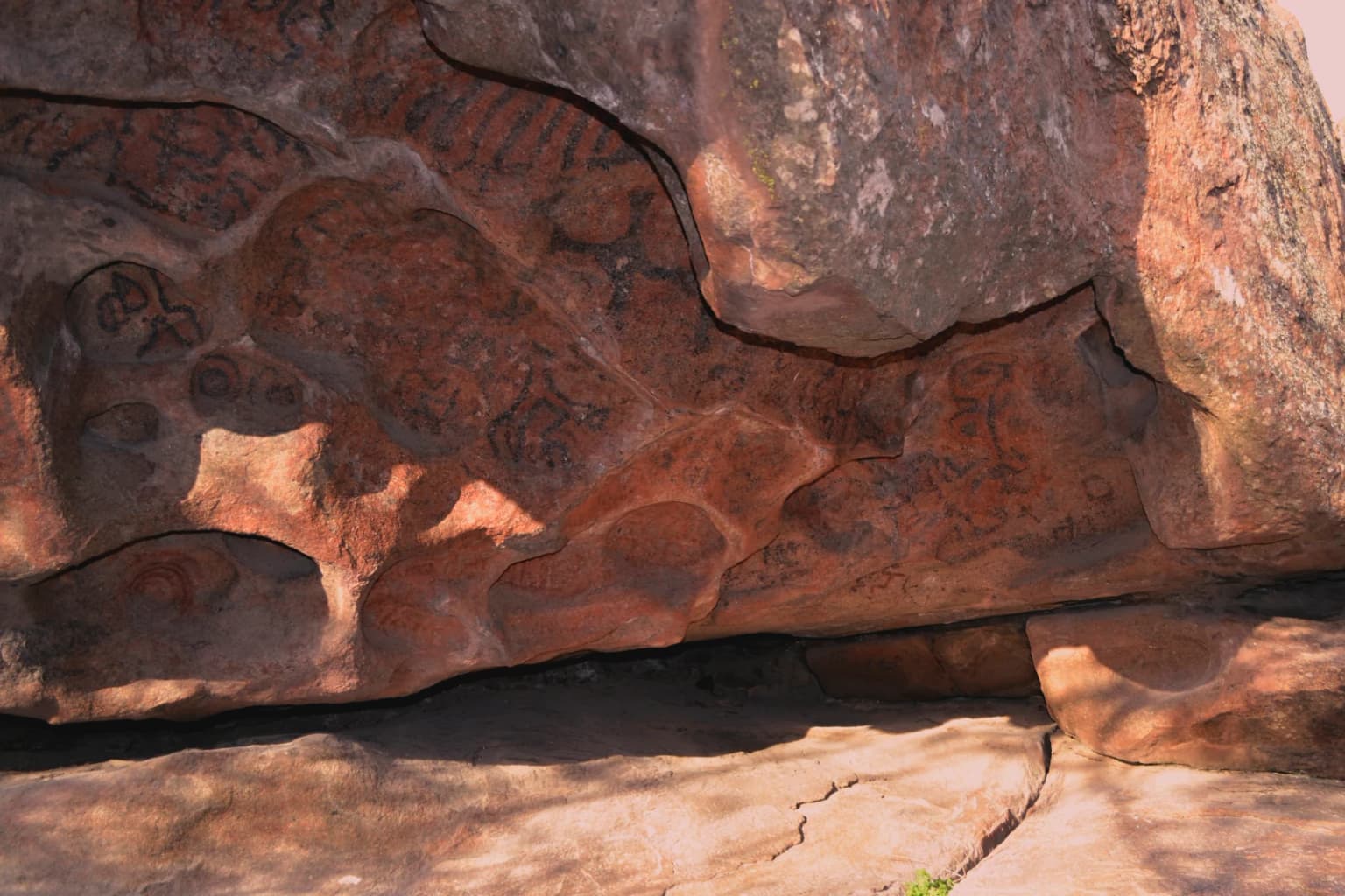 Rock face with ancient reddish-brown cave paintings featuring abstract designs and patterns
