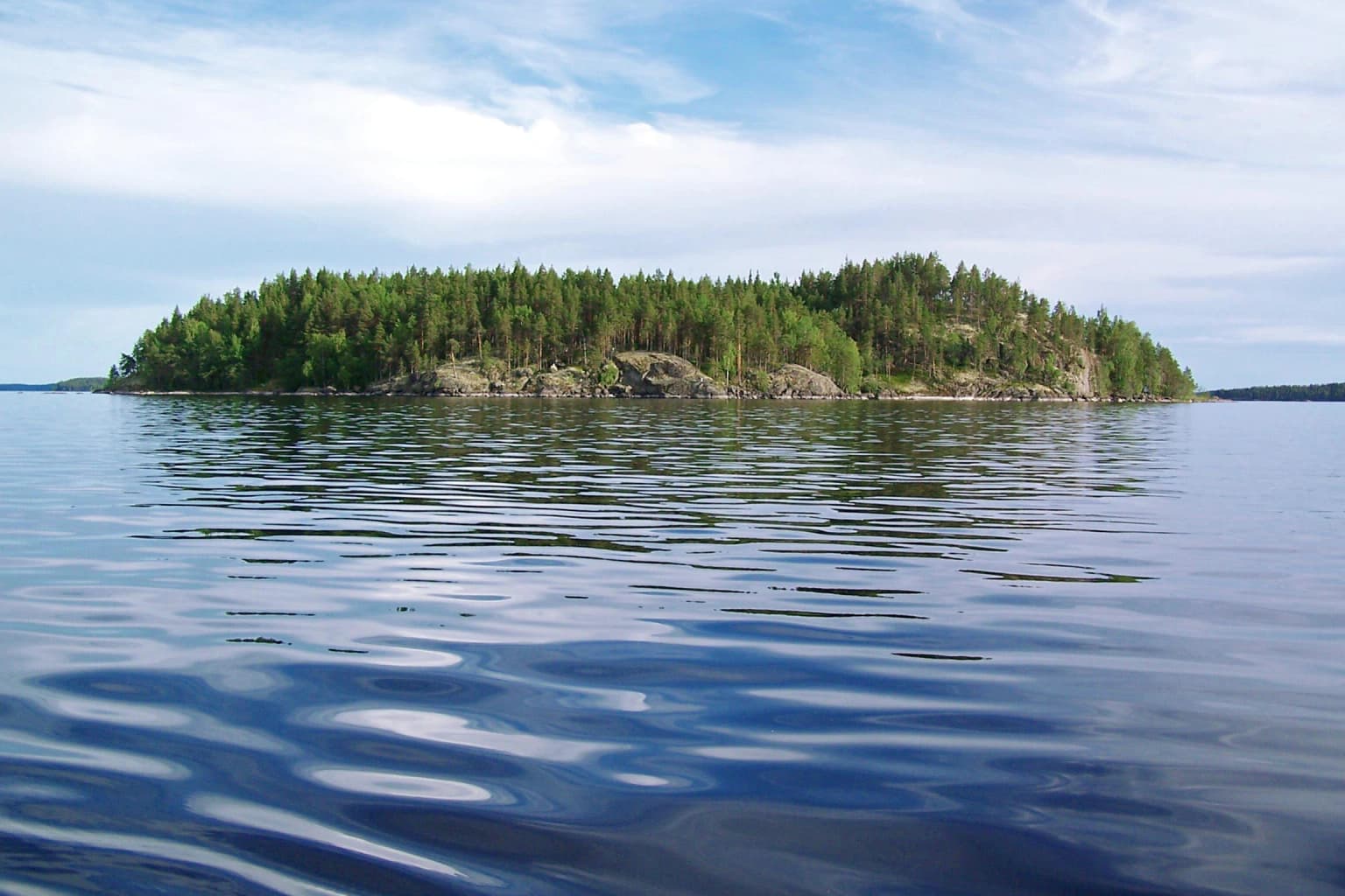 Forest-covered island surrounded by calm blue water under a partly cloudy sky
