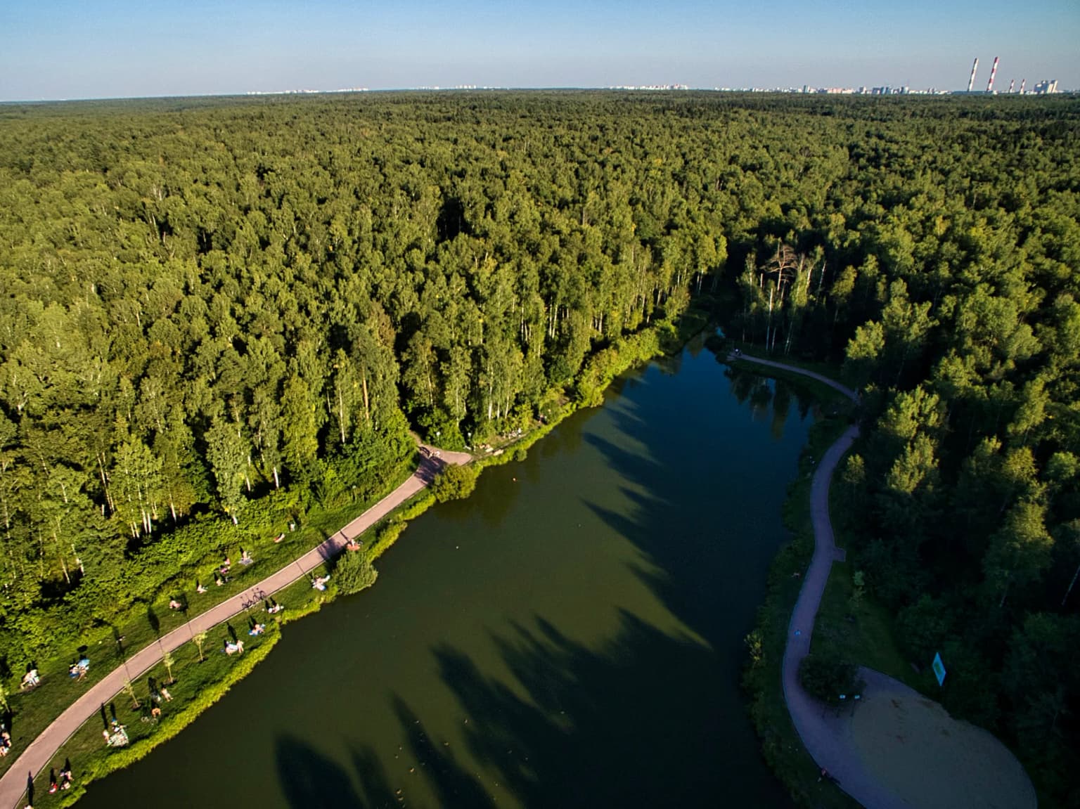 Aerial view of a large pond surrounded by dense green forest with winding paths along the shore