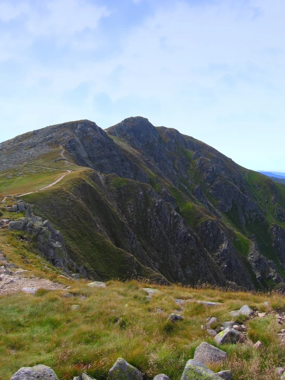 A mountain peak with rocky slopes and grassy terrain under a partly cloudy sky