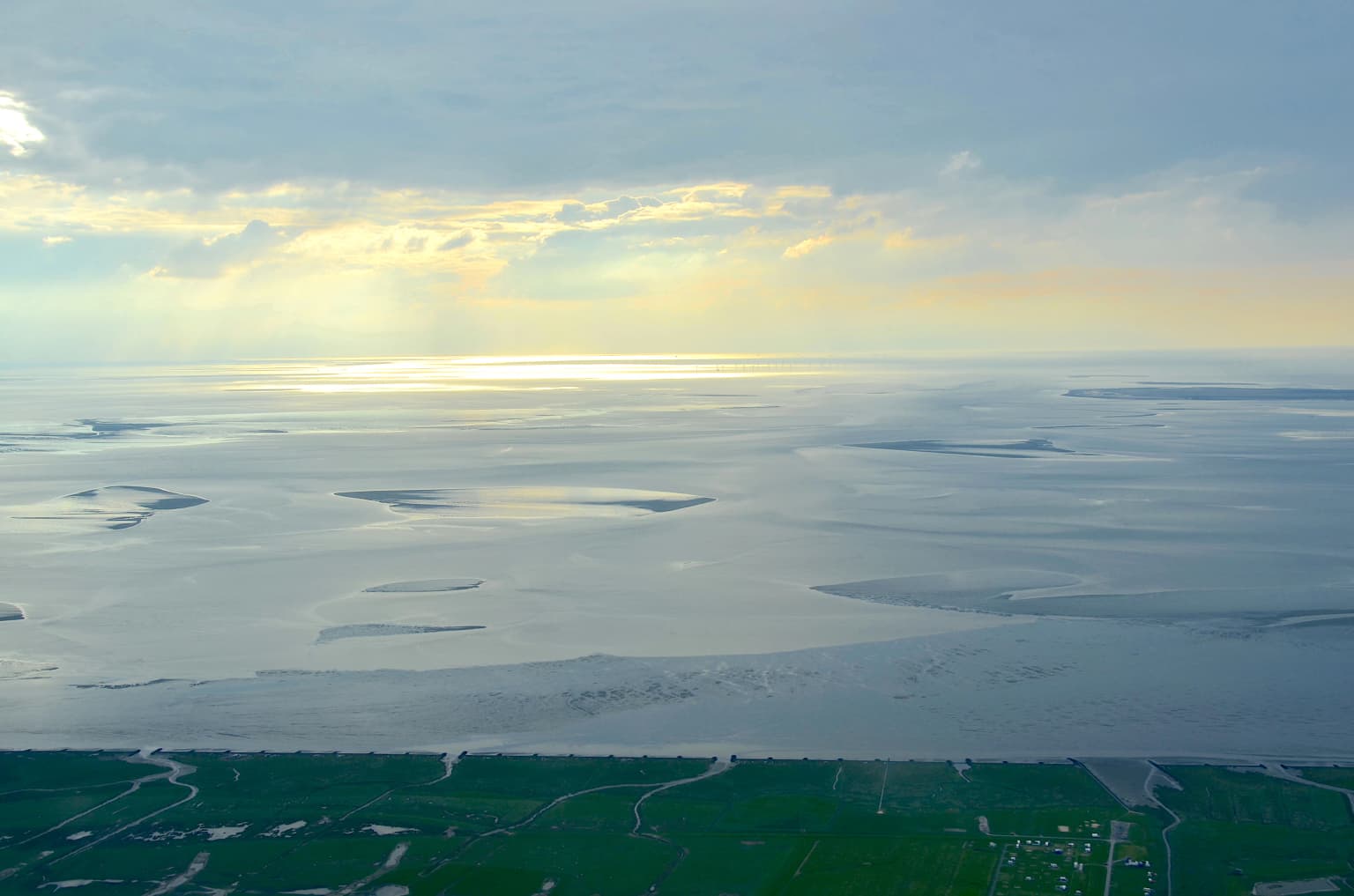 Aerial view showing extensive sandbanks and tidal flats in the Lower Saxon Wadden Sea National Park with coastal vegetation in the foreground