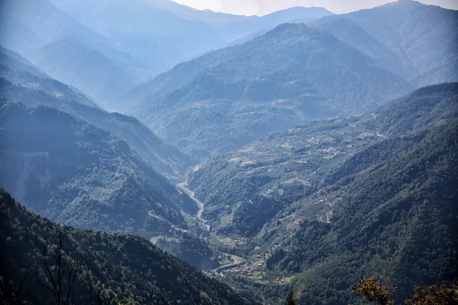 Wide valley view with mountain ranges, forested slopes, and a winding river in the distance