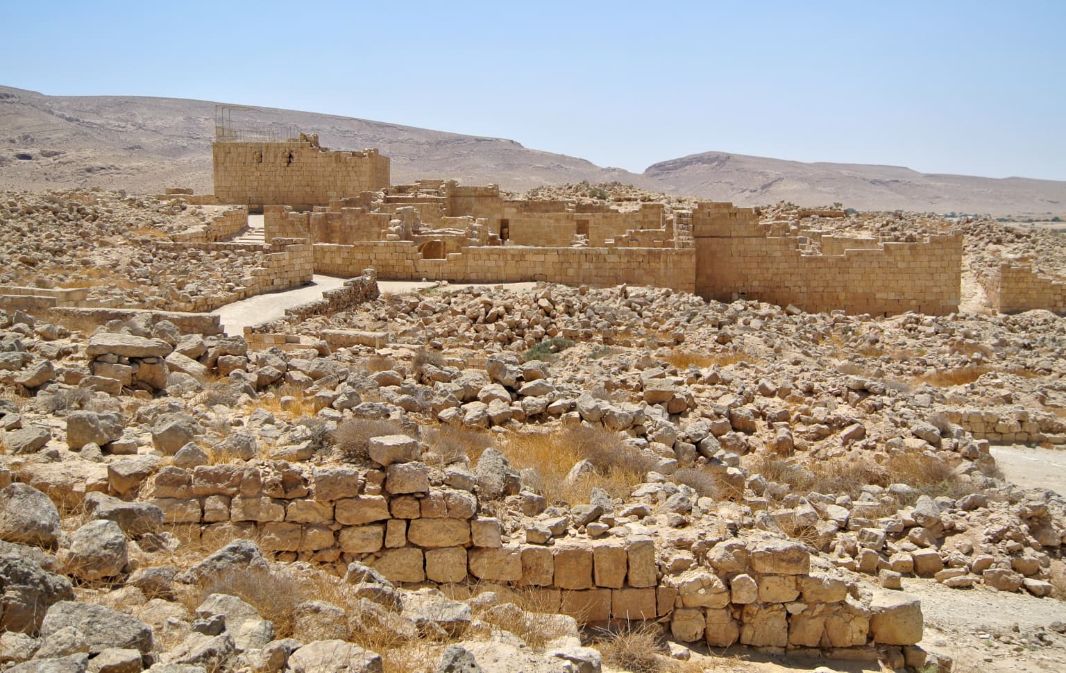 Estructuras de piedra en ruinas en un paisaje desértico con muros y cimientos antiguos
