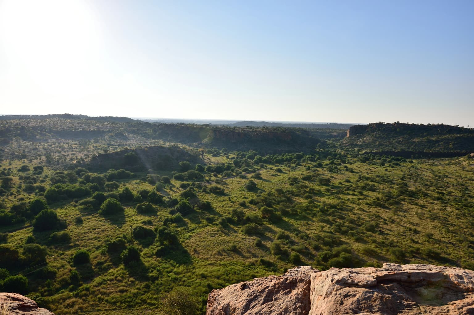Wide landscape of Limpopo River valley with green savanna vegetation and rocky outcrops under clear blue sky
