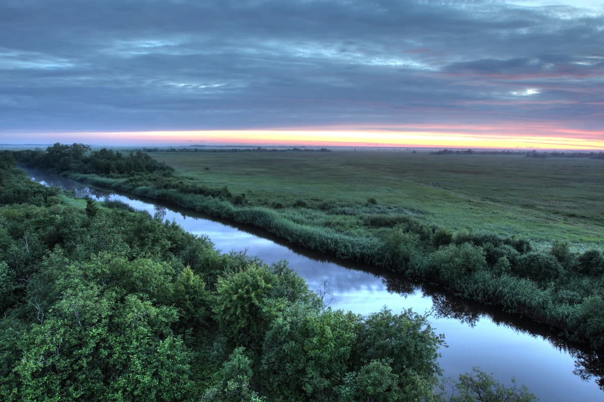 A river winding through a lush green landscape under a cloudy sky with sunset hues on the horizon