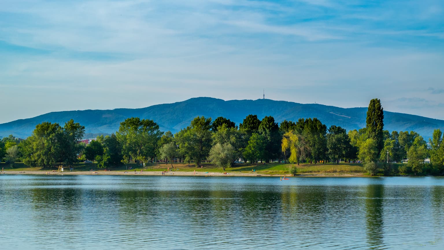 Calm lake reflecting trees and Medvednica mountain under a clear blue sky