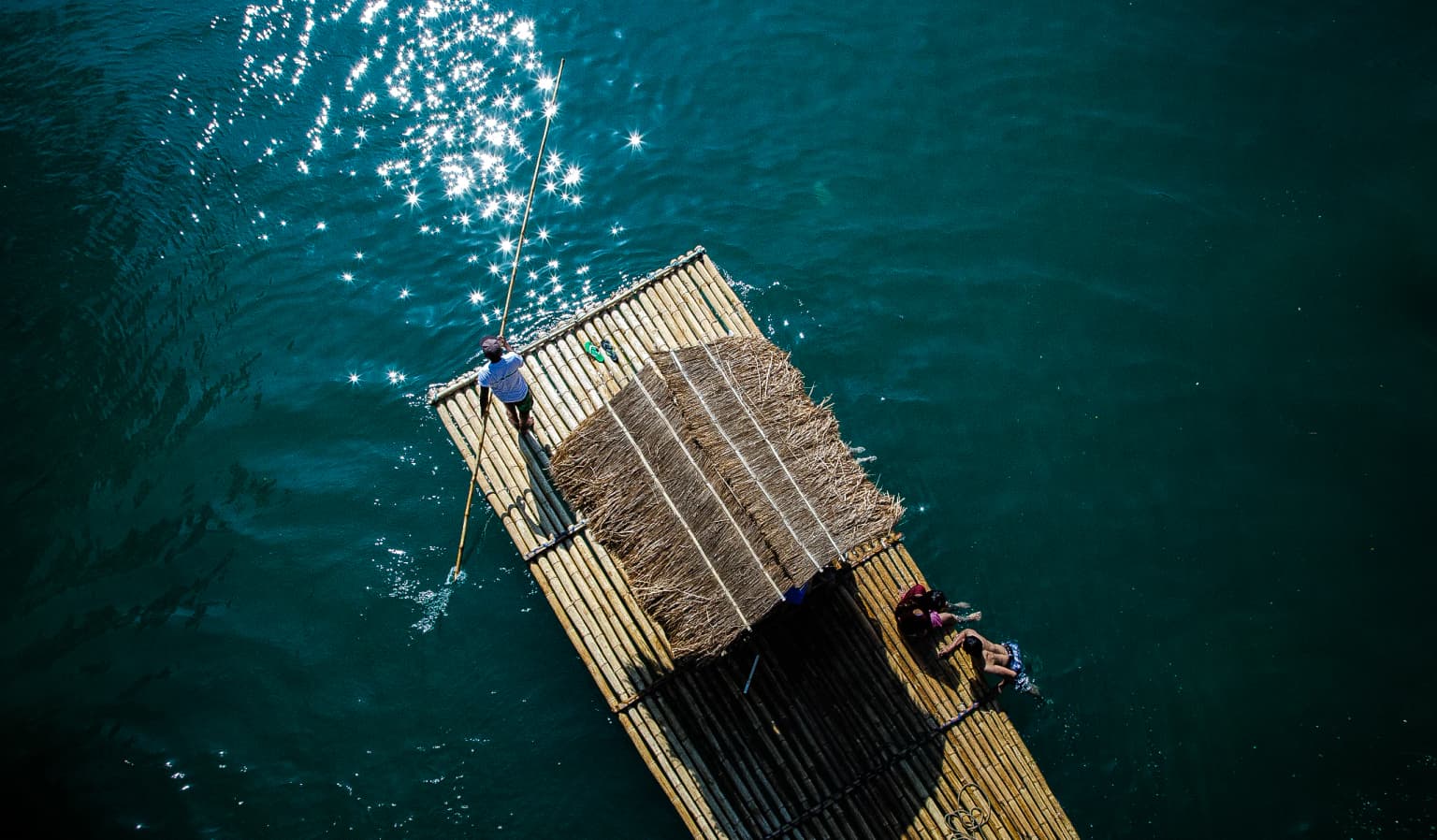 Aerial view of a bamboo raft with two people navigating the river using a pole