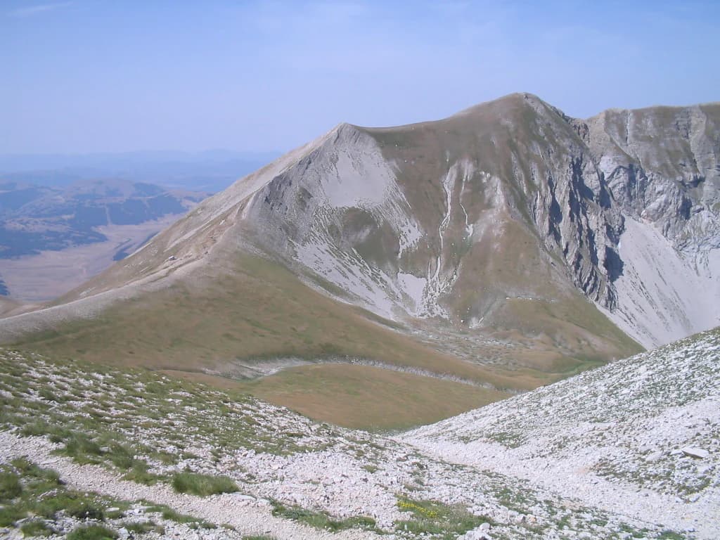 Mountain peak with rocky slopes and grassy terrain under a clear blue sky
