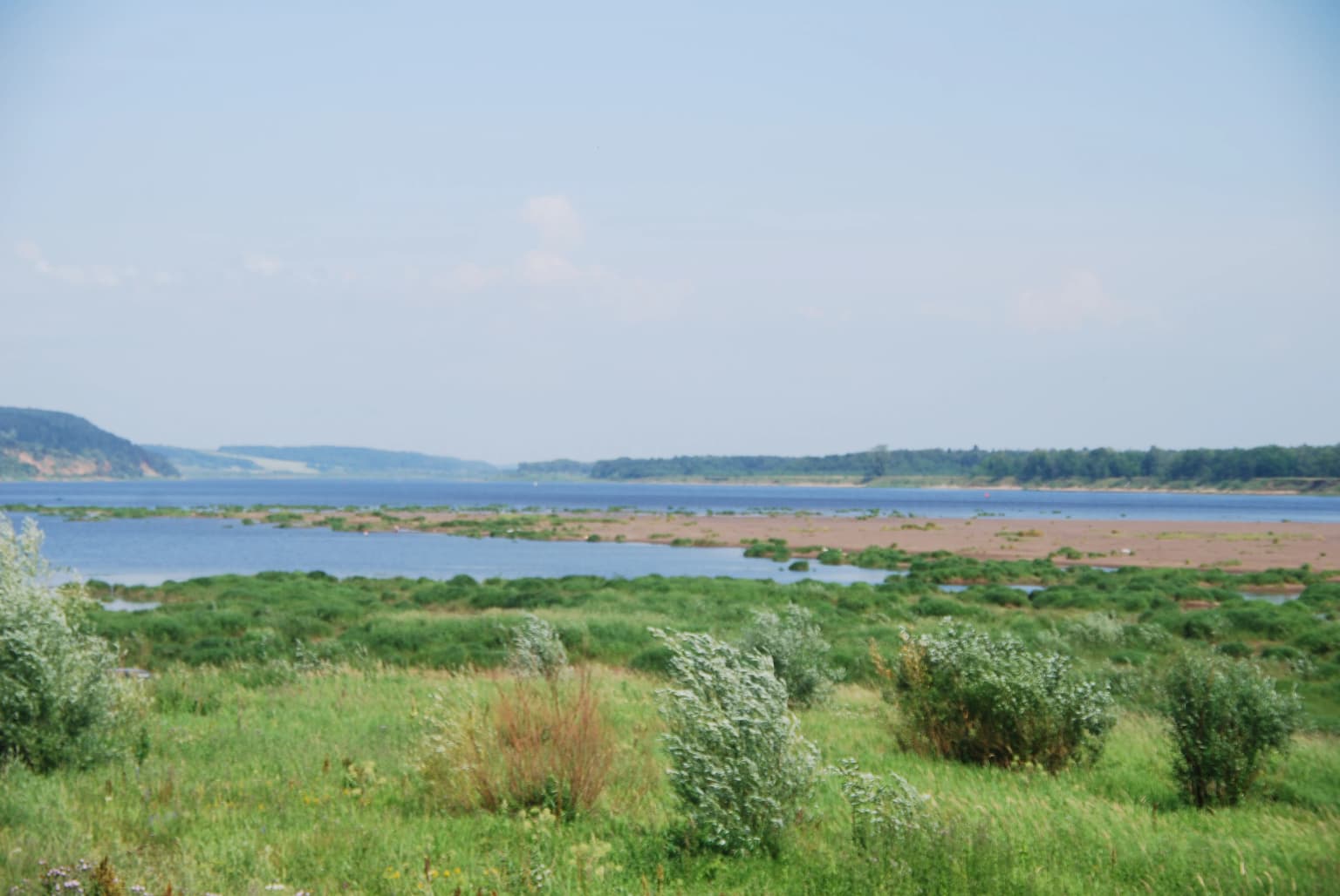 Wide landscape view of Kama River with green vegetation and distant hills under clear sky