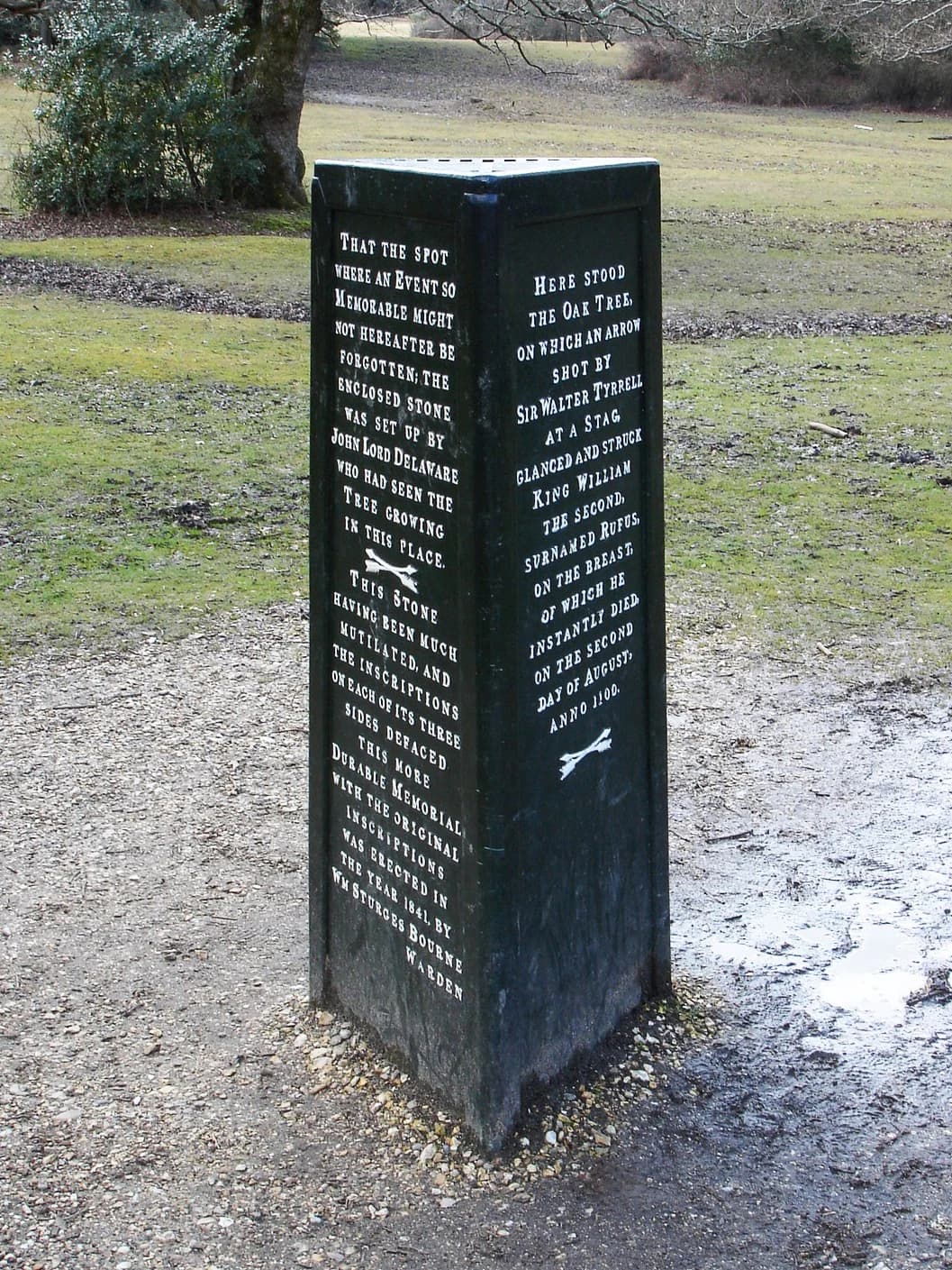Dark stone monument with engraved historical text, situated in a grassy field with trees in the background