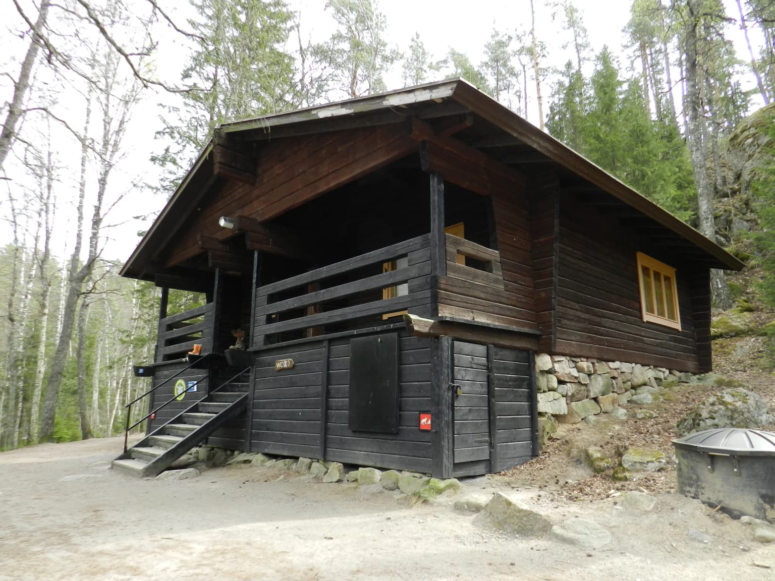 Wooden guide hut with stone foundation and staircase, surrounded by forest, located in Nuuksio National Park