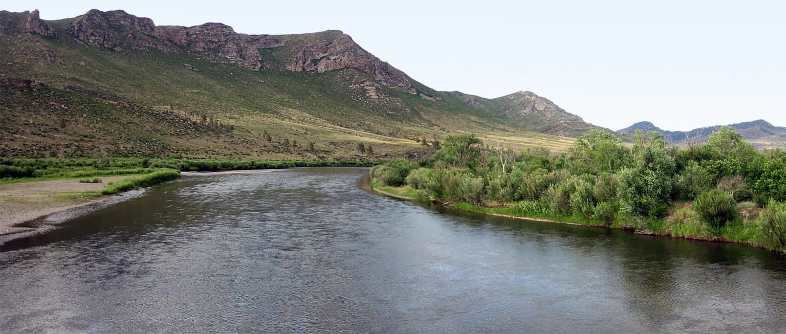 Río que fluye a través de un valle rodeado de vegetación verde y montañas a lo lejos
