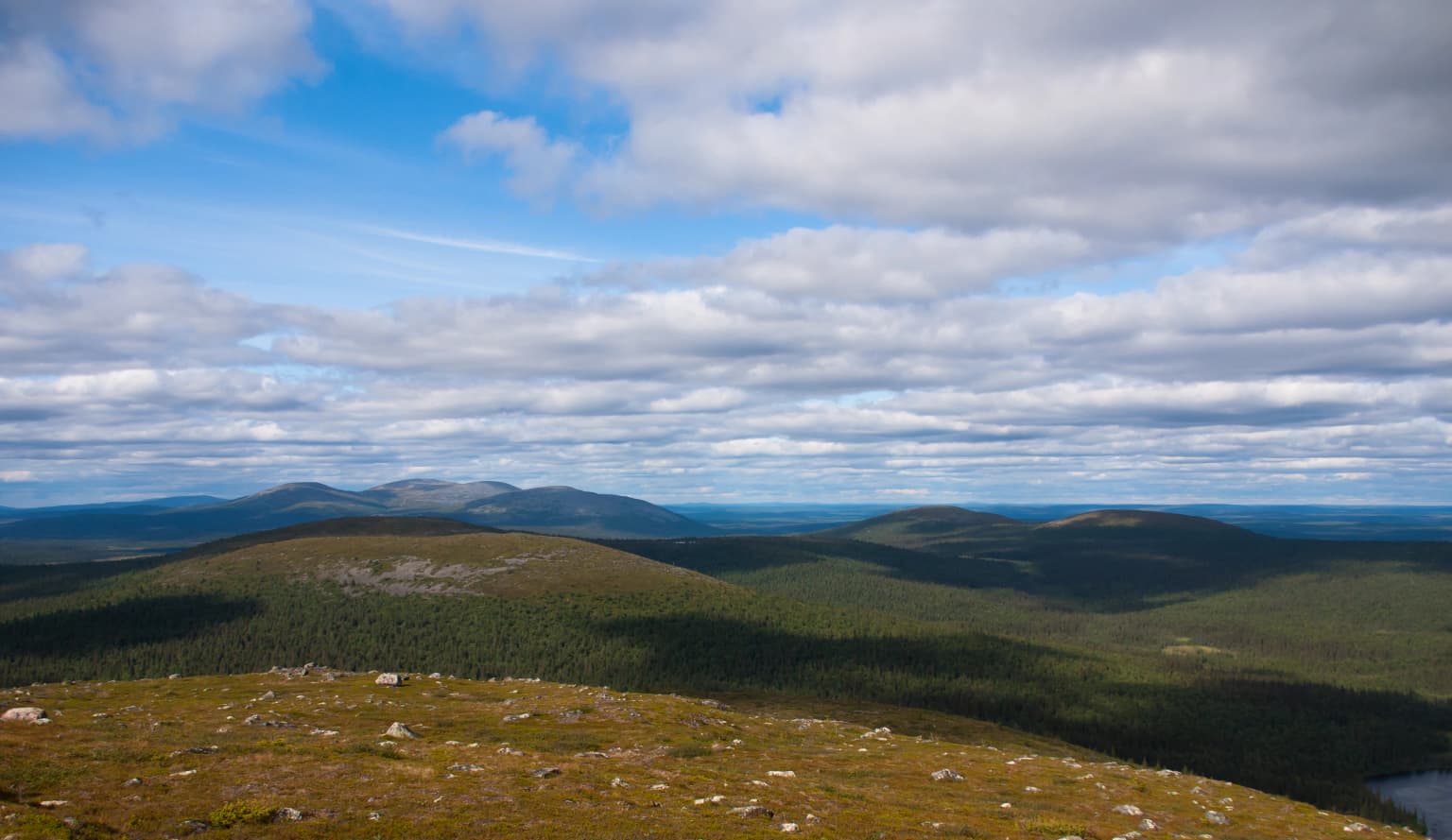 Wide landscape view showing rolling hills, forested areas, and a partly cloudy sky