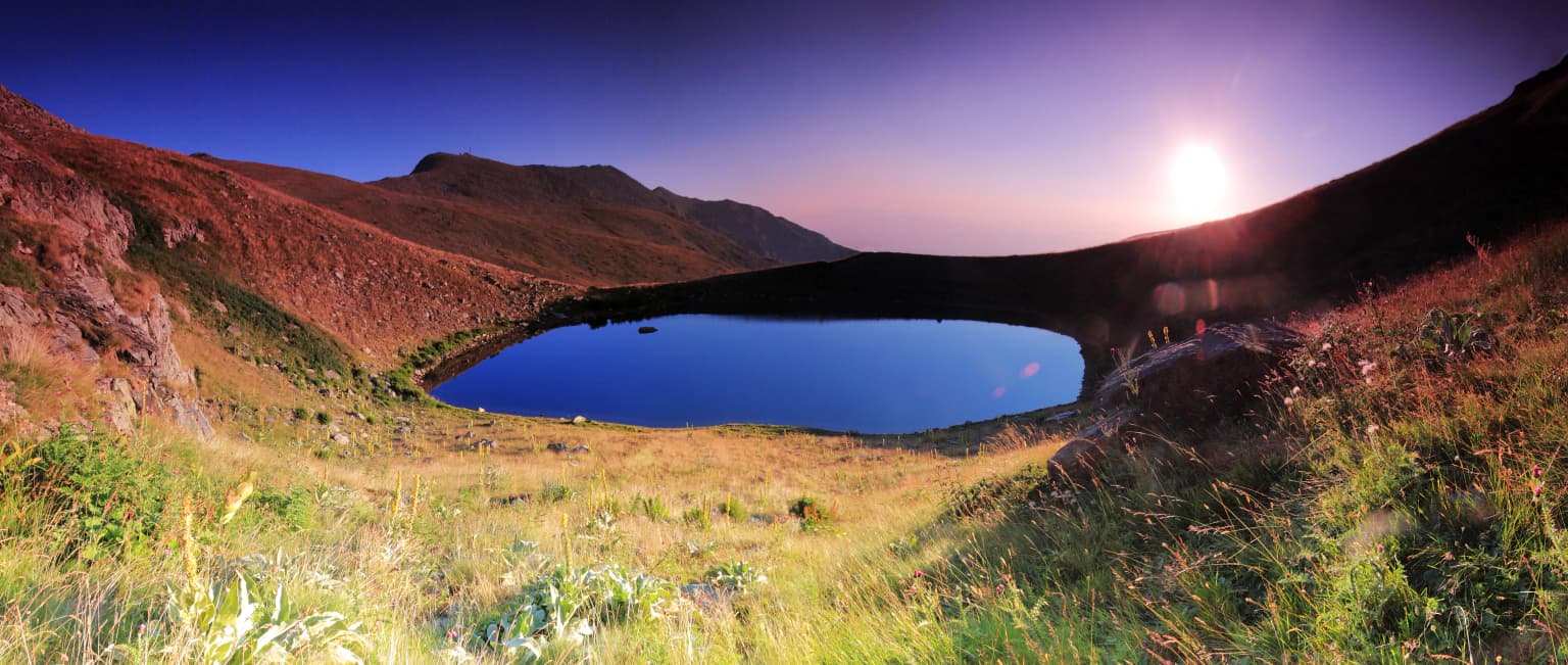 Panoramic view of Malo Ezero at sunrise with grassy hills and mountain slopes under a gradient sky transitioning from deep blue to purple
