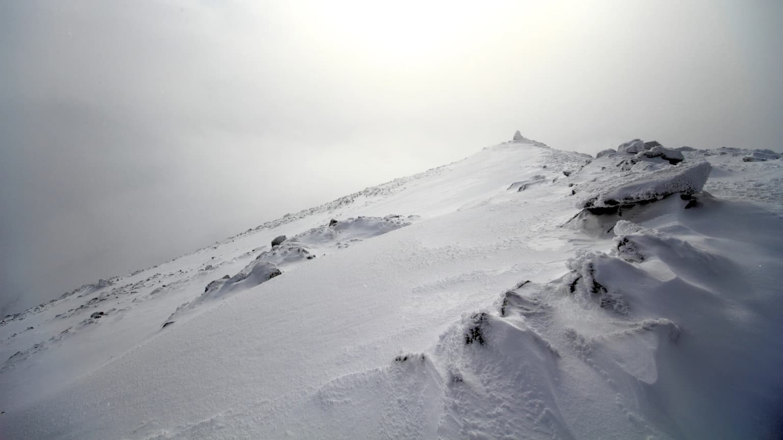 Snow-covered mountain ridge under overcast sky with minimal visibility