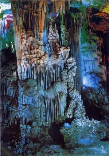 Interior of Tien Son Cave with hanging stalactites and formations on cave walls and floor, illuminated with blue and green lighting