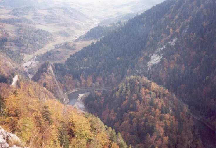 Wide landscape view of a river flowing through mountain valleys surrounded by autumn-colored forests
