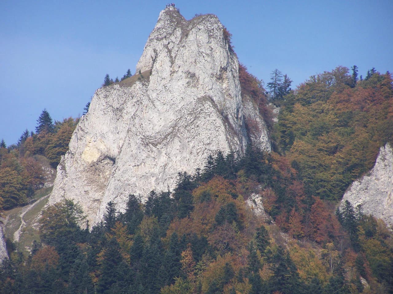 Rocky mountain peak with autumn-colored forest under clear blue sky