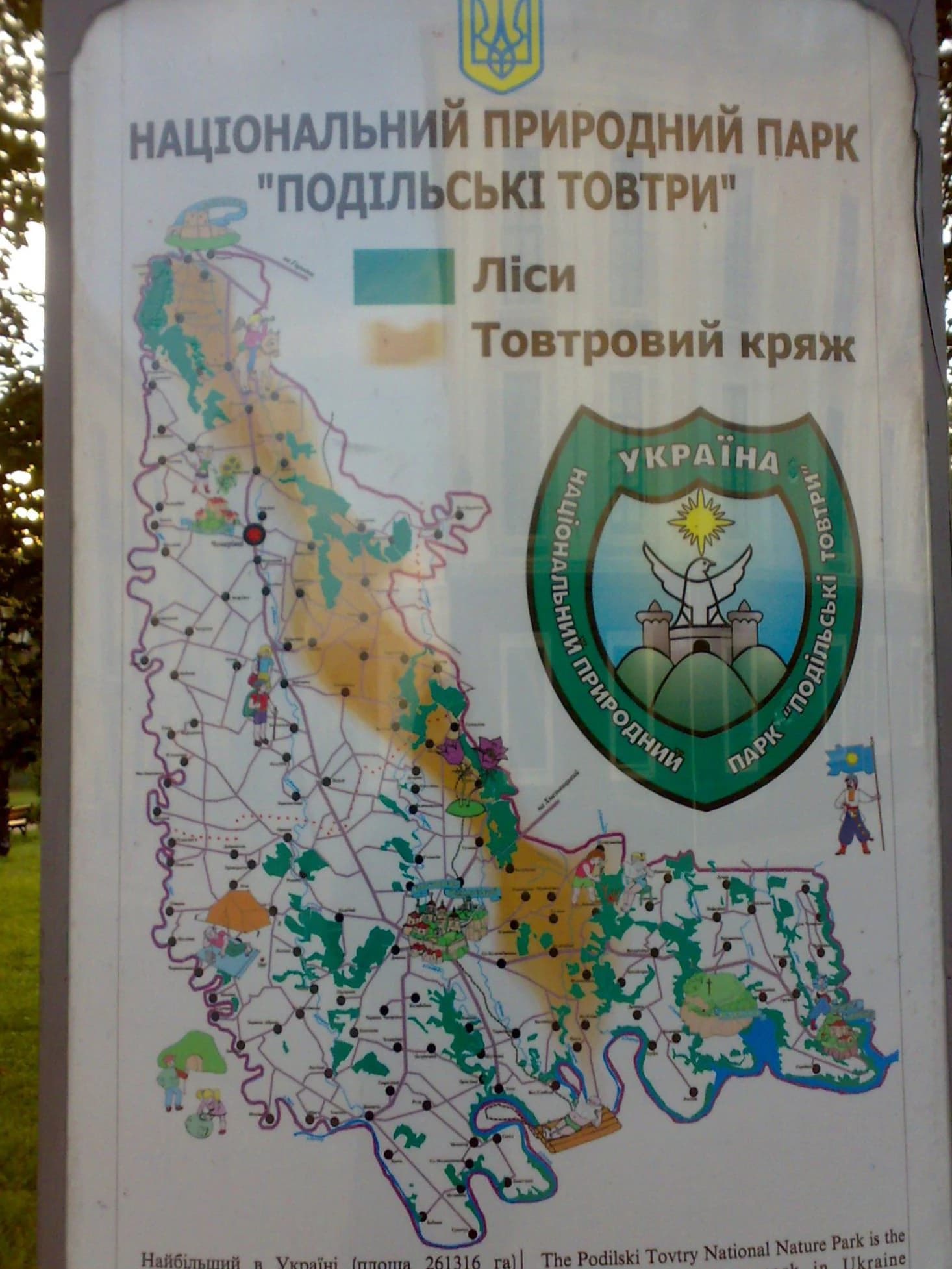 Ukrainian-language information sign for Podilski Tovtry National Nature Park showing a park map, emblem, and text labels including 'Ліси' and 'Товтровий кряж'
