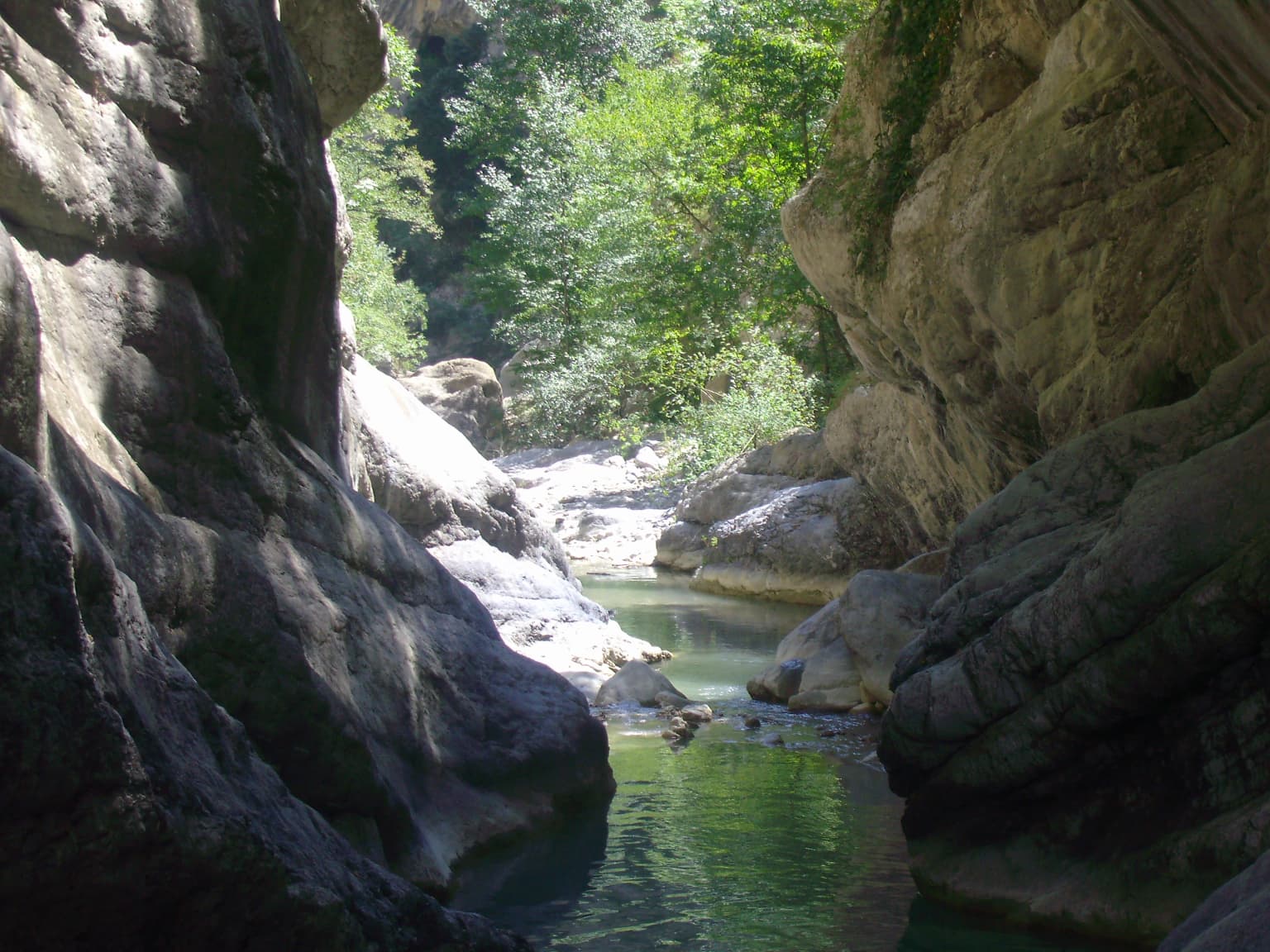 A narrow gorge with steep rocky cliffs and a calm river flowing through, surrounded by green vegetation