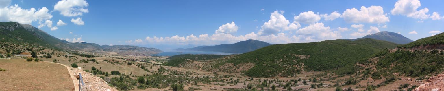 Panoramic landscape of Prespa National Park showing Lake Prespa, green mountains, and open valleys under a clear blue sky with scattered clouds