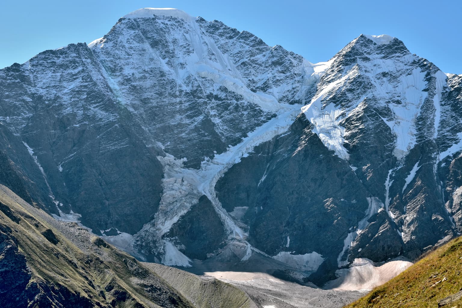 A mountain landscape with snow-covered peaks and glaciers under a clear blue sky