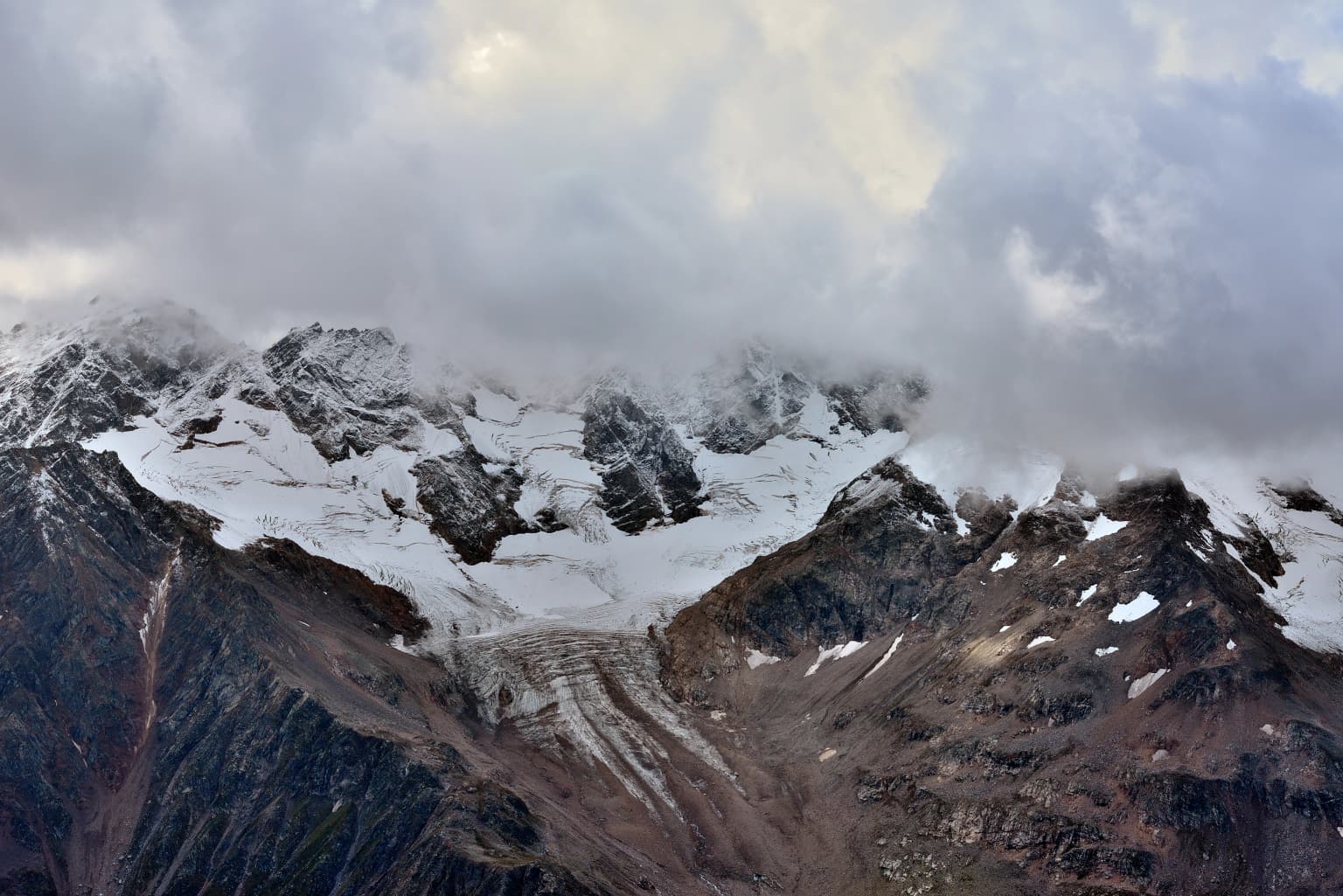 Snow-covered mountain peaks with glacier visible in the mid-ground, partially obscured by clouds