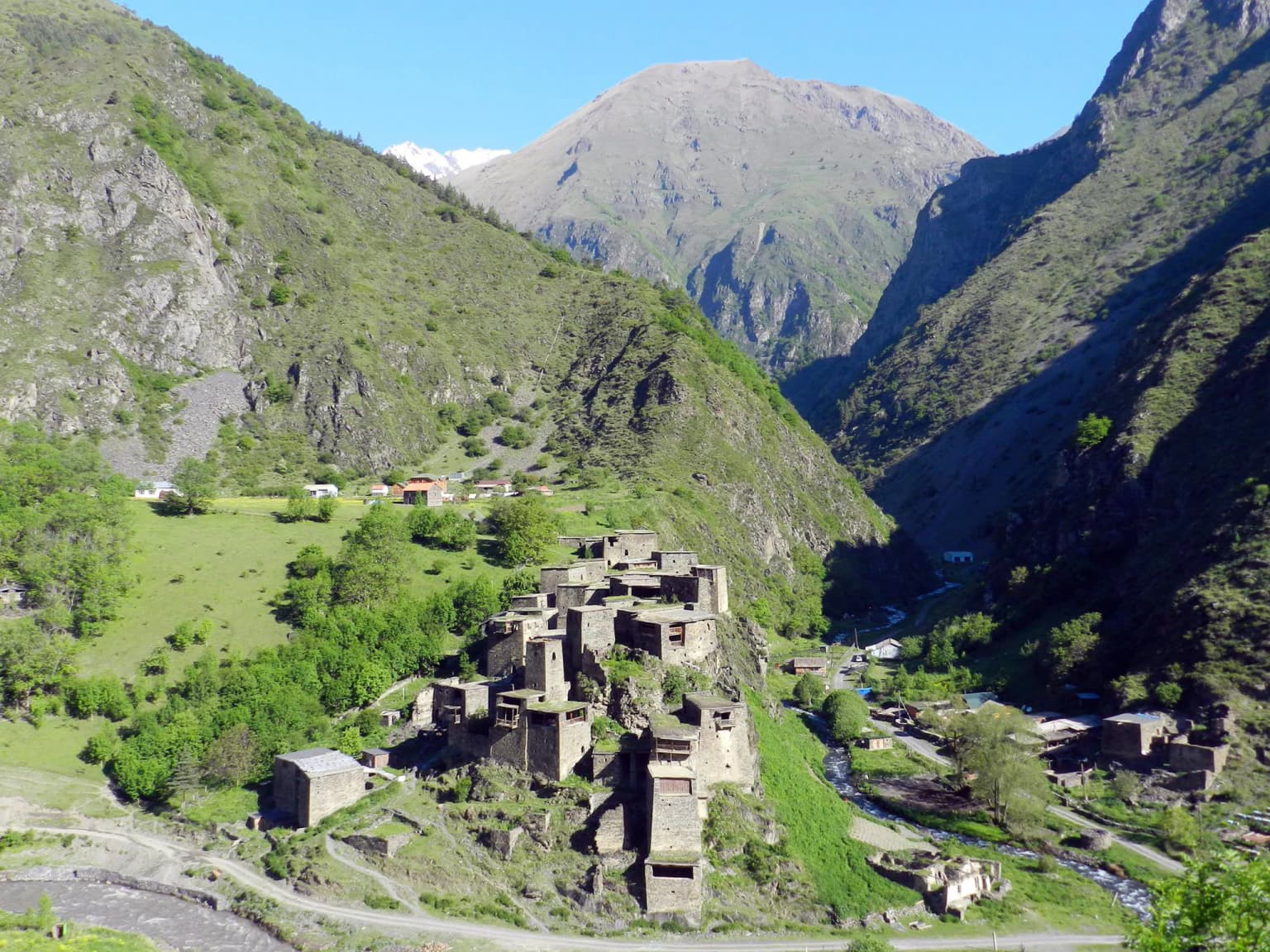 Stone buildings of Shatili village in a mountain valley with green slopes and distant mountains