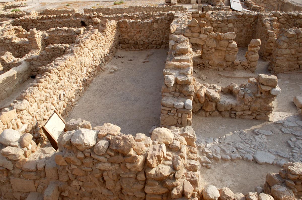 Ruinas de estructuras antiguas de piedra con muros y cimientos en un entorno desértico, incluyendo un cartel informativo