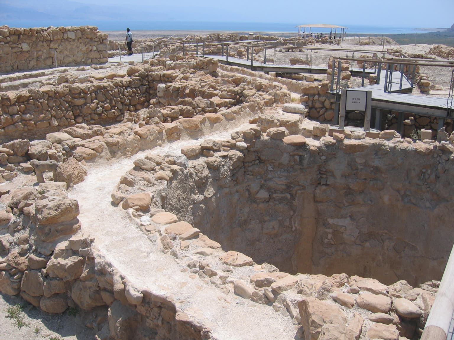 Estructura de cisterna de piedra con ruinas antiguas circundantes y una persona de pie al fondo