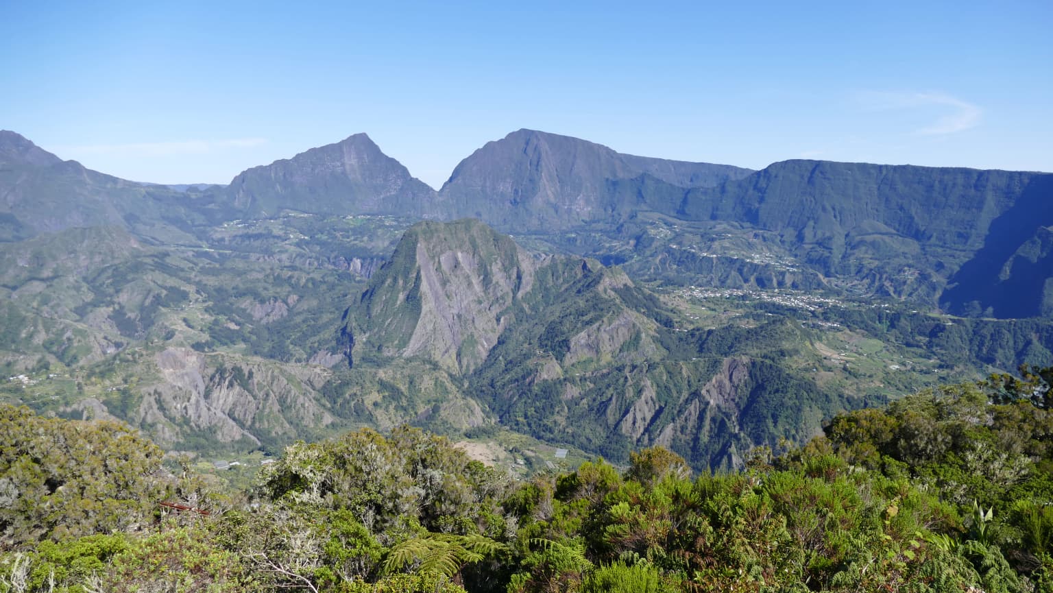 Mountainous landscape with deep valleys and lush green vegetation under a clear blue sky