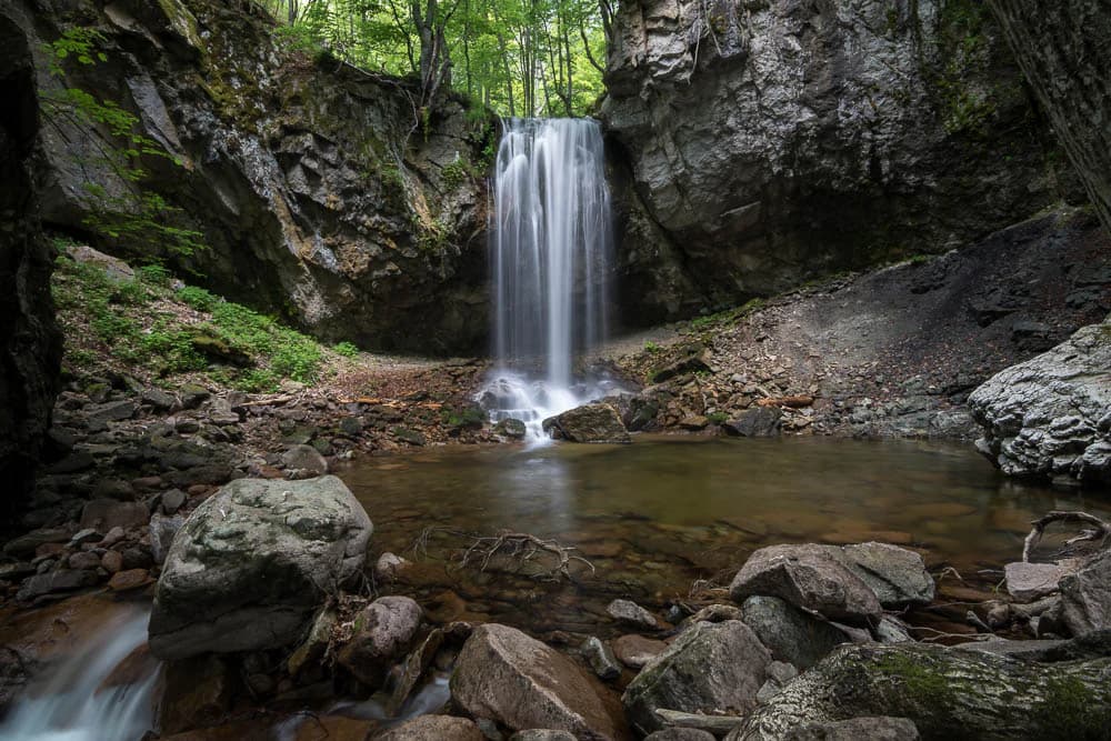 Waterfall cascading over rocks into a pool surrounded by forest and boulders