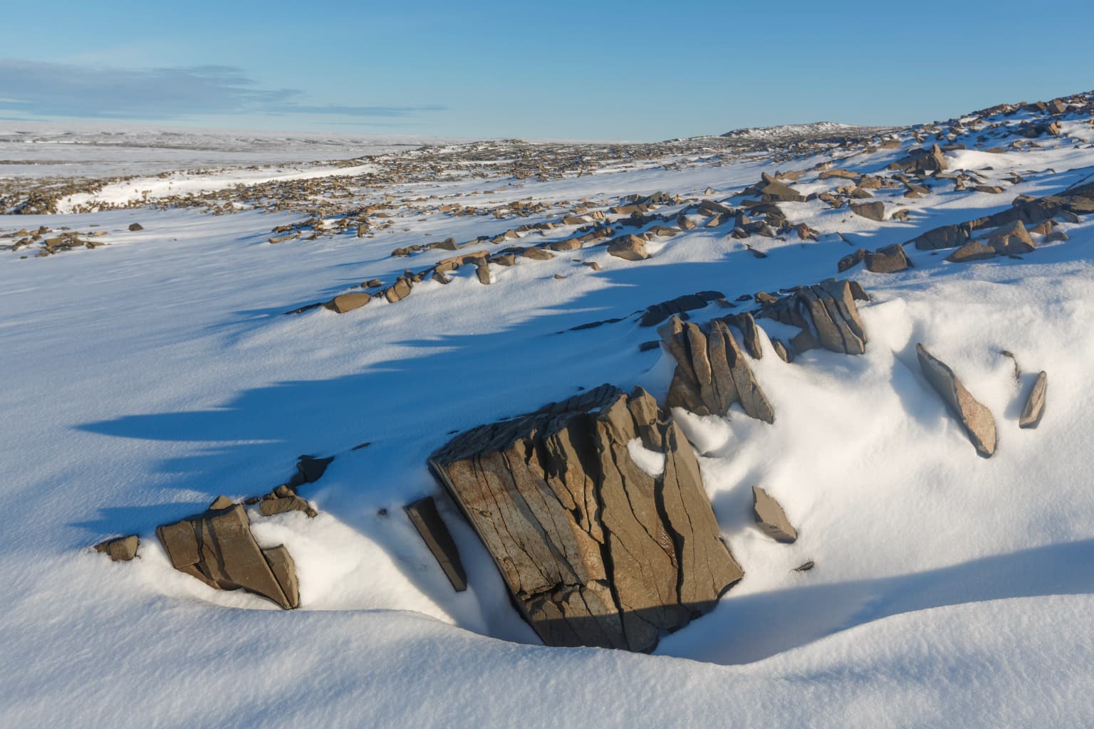 Snow-covered terrain with exposed rocky outcrops under a clear blue sky