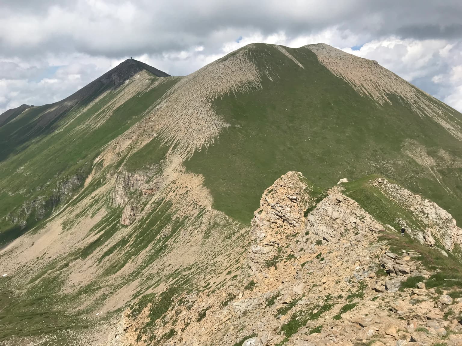 Two prominent mountain peaks with rocky slopes and green vegetation under a partly cloudy sky