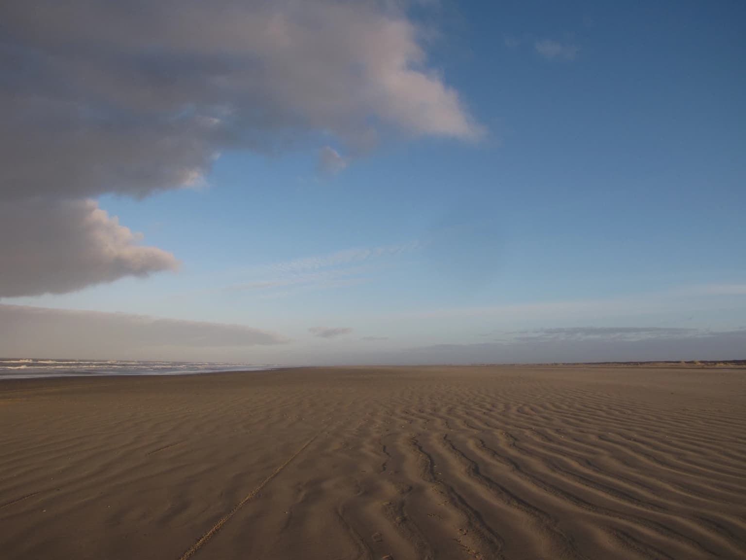 Sandy beach with rippled patterns extending toward the ocean under a partly cloudy sky