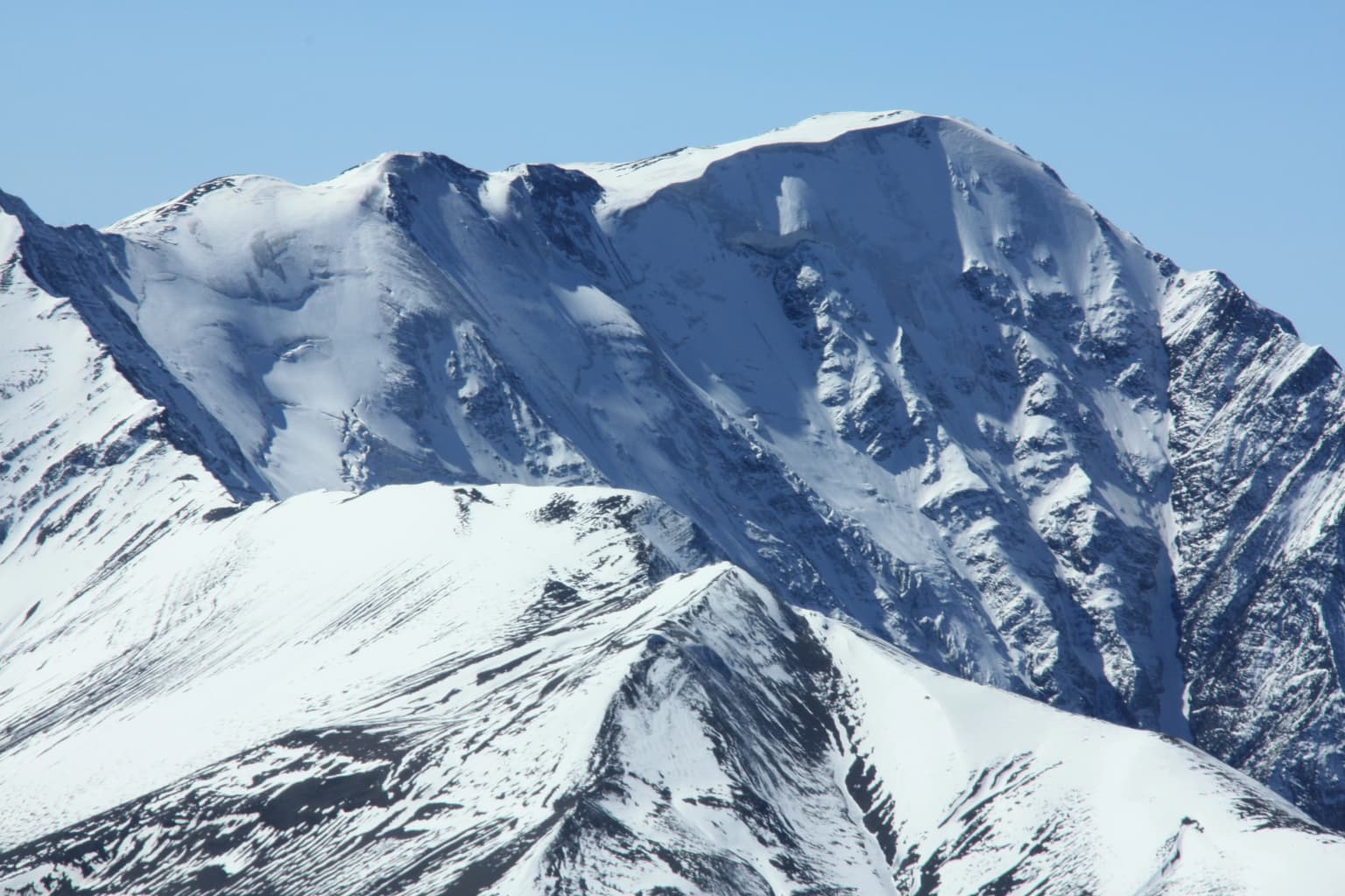 Snow-capped mountain peak with rugged terrain under clear blue sky